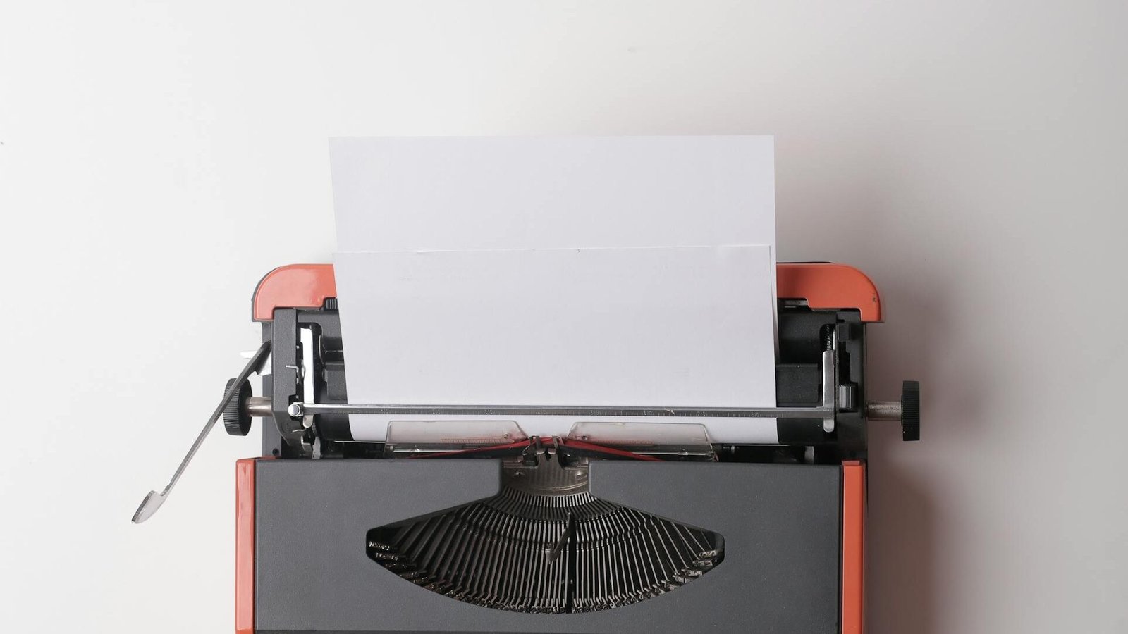 From above crop person using vintage black and red typewriter with white blank sheet of paper against white background